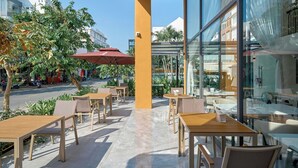 A cafe with outdoor seating, a glass wall, and a view of the street. - BALVENIE HOTEL Phu My Hung SECC (Ho Chi Minh City)