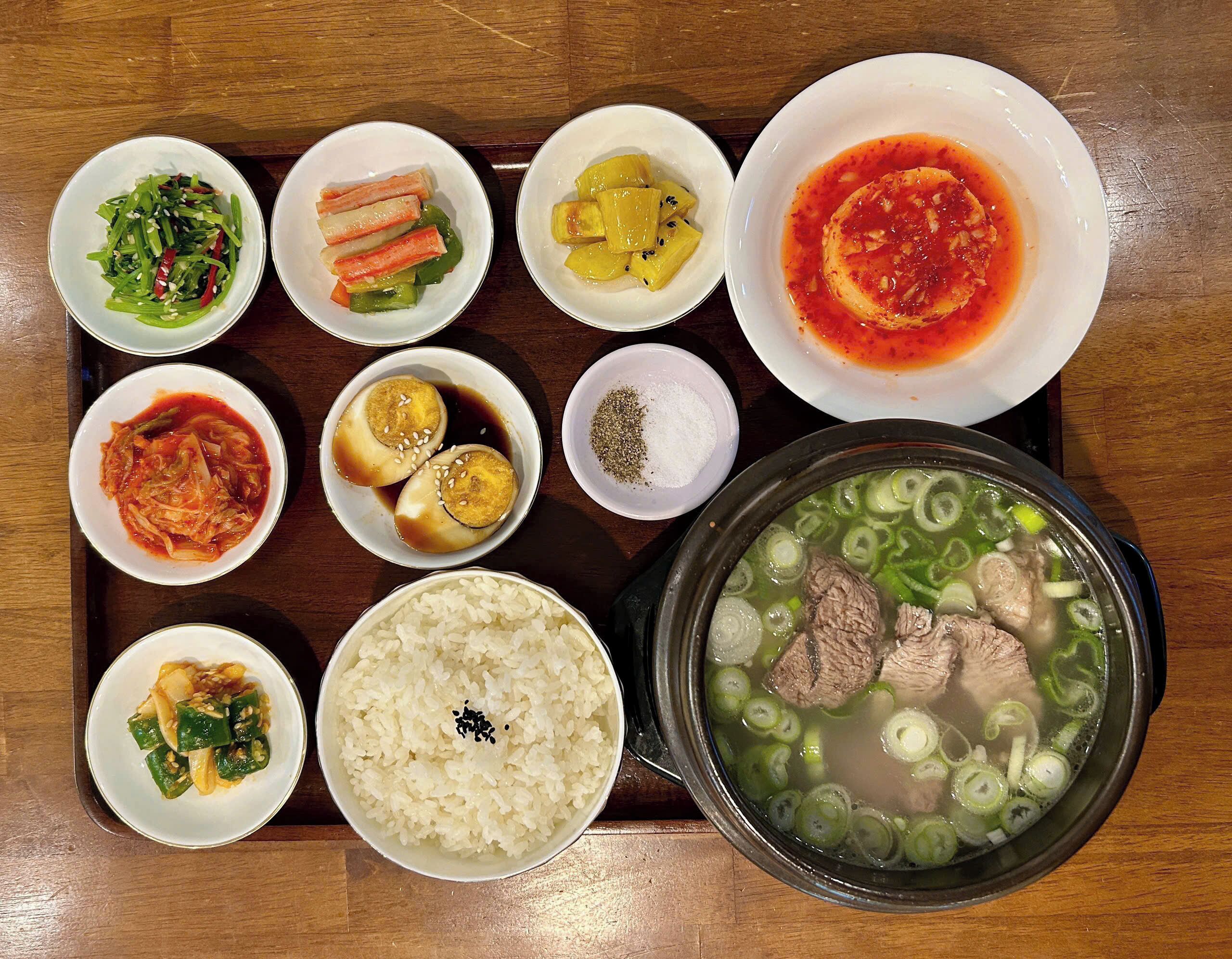 On vous proposera un assortiment de plats, notamment un bol de soupe contenant de la viande et des légumes, une assiette de riz et plusieurs petits plats avec différents types d’aliments.