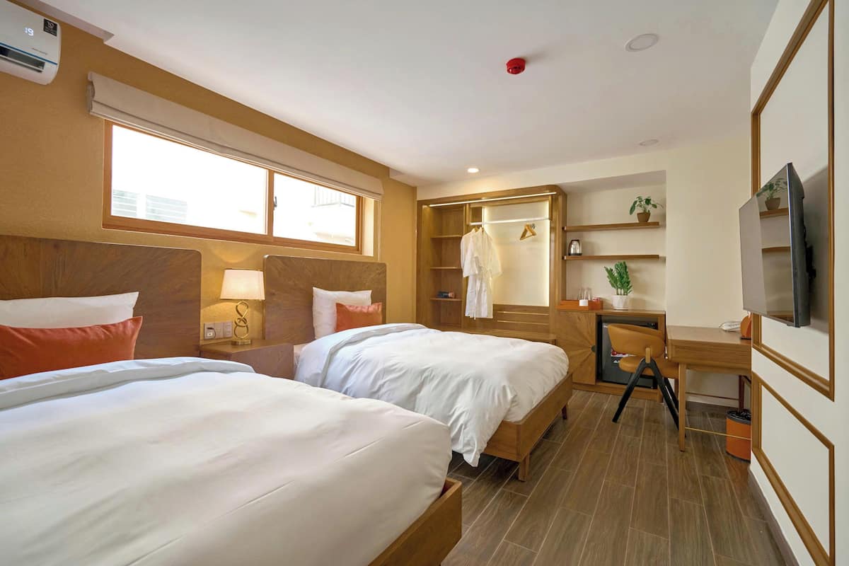 A hotel room with two beds, a desk, a TV, a wardrobe, and a window.
