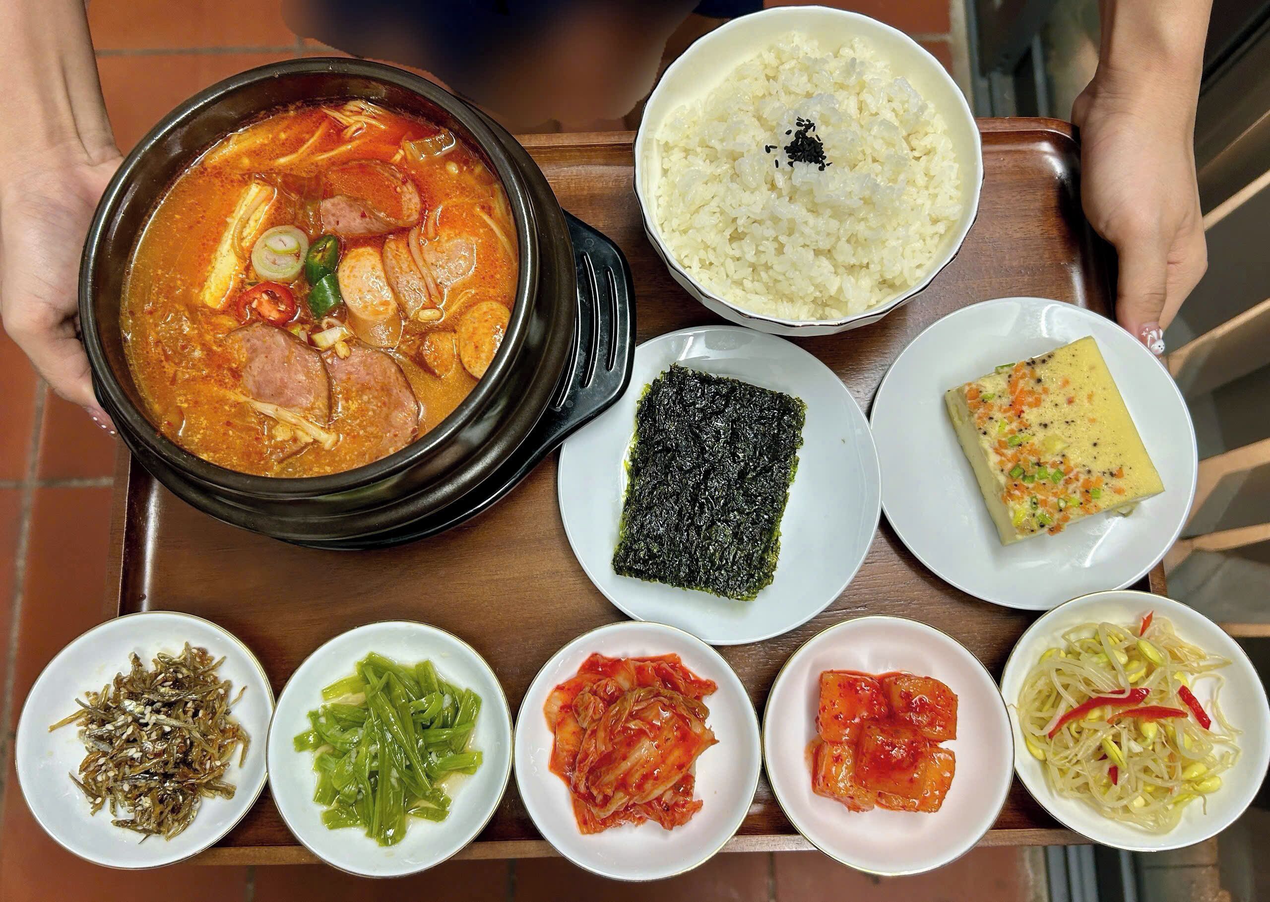 A tray with various Korean dishes including a bowl of soup, rice, seaweed, and several side dishes.