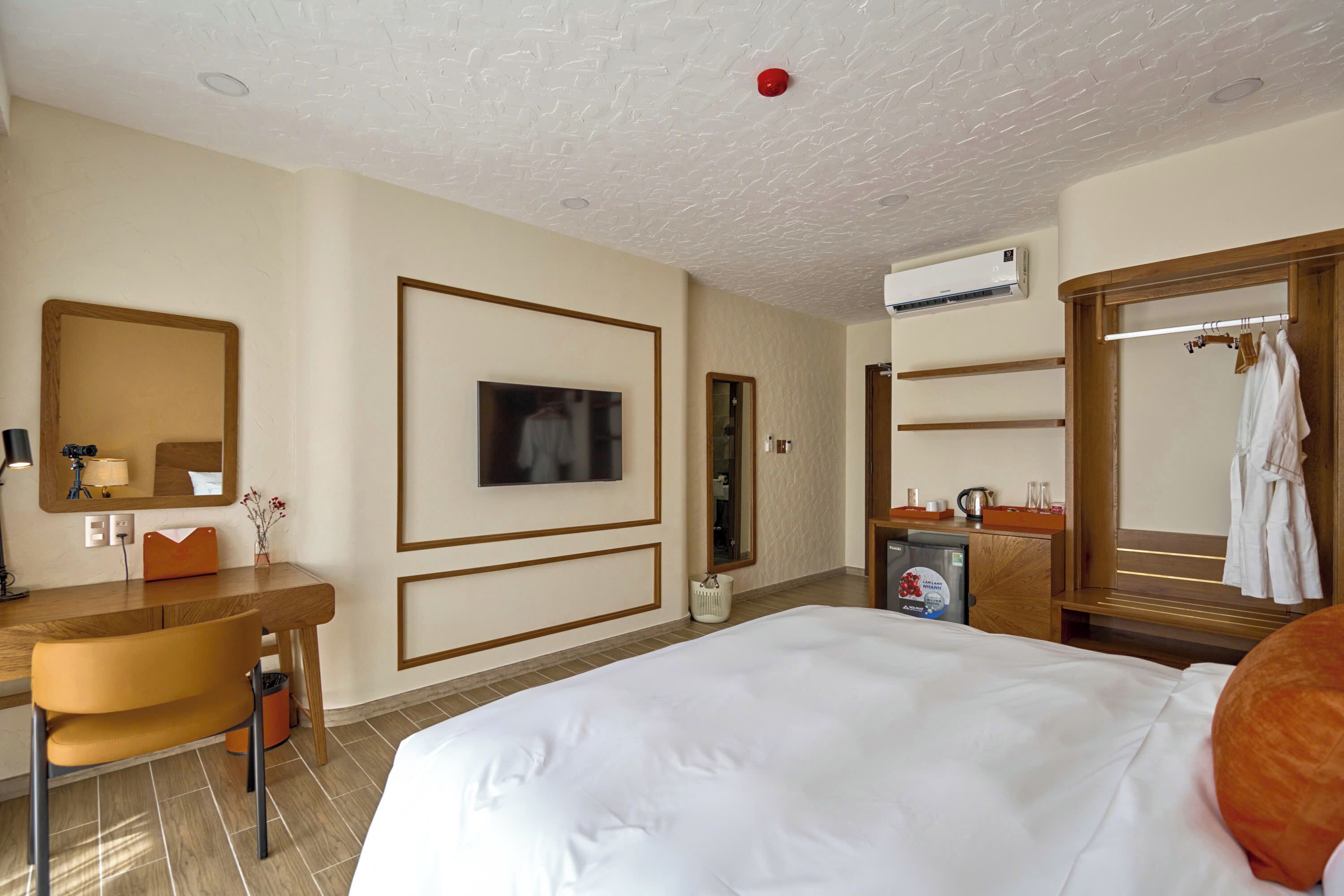 Ein Hotelzimmer mit Bett, Schreibtisch, Stuhl, Fernseher, Spiegel, Kleiderschrank und Klimaanlage.