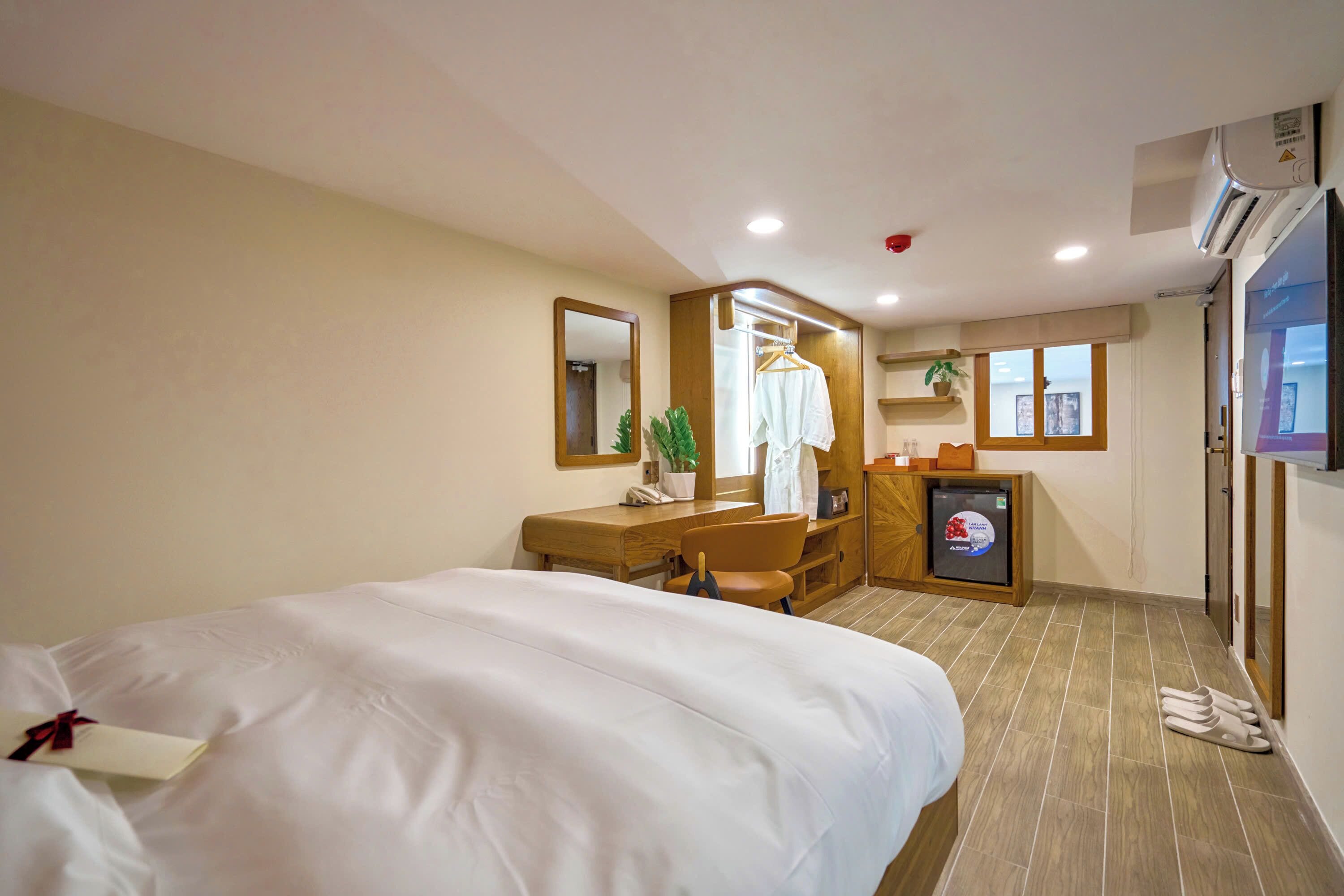 A hotel room with a large bed, a desk with a chair, a small kitchenette, and a mirror.