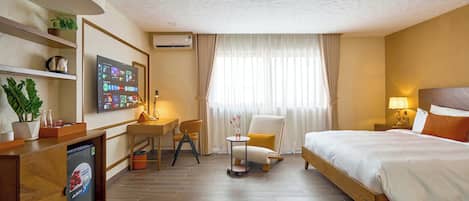 Habitación de hotel con cama, escritorio con silla, televisor, una mesita de noche con lámpara y una planta en maceta.