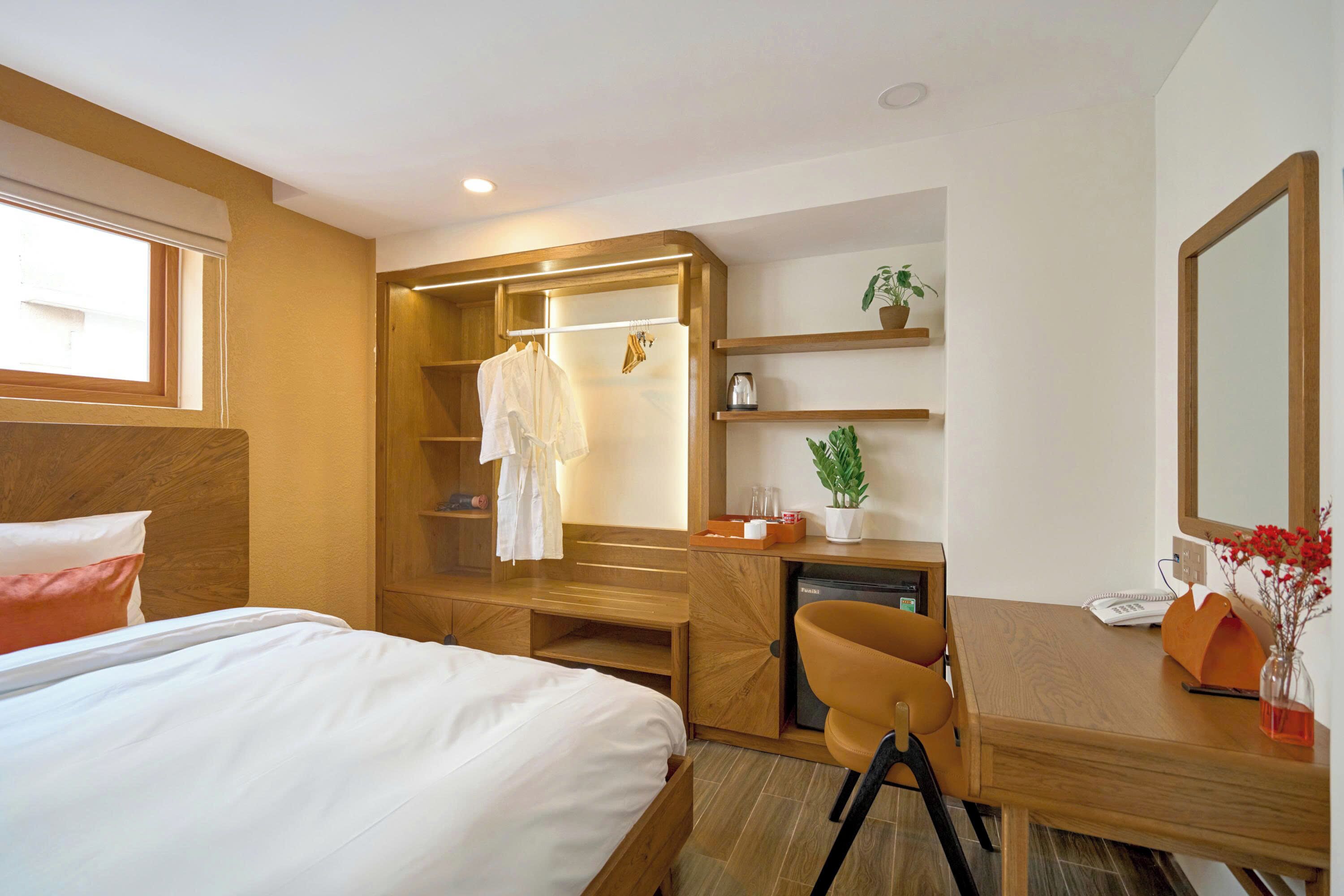 A hotel room with a bed, a desk, a chair, a wardrobe, and a small plant.