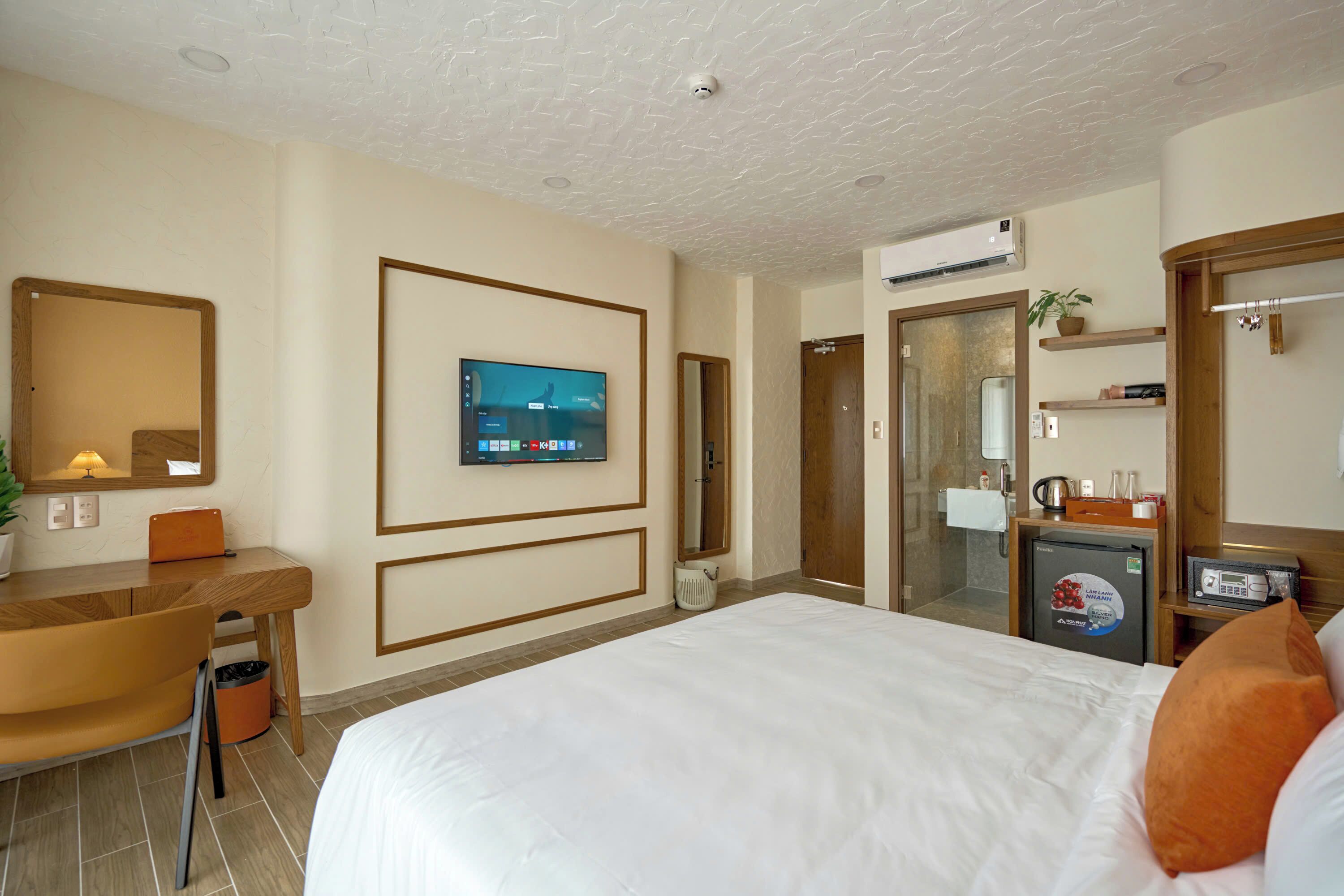 A hotel room with a bed, a desk, a television, a mirror, and a small refrigerator.