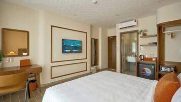 A hotel room with a bed, a desk, a television, a mirror, and a small refrigerator.