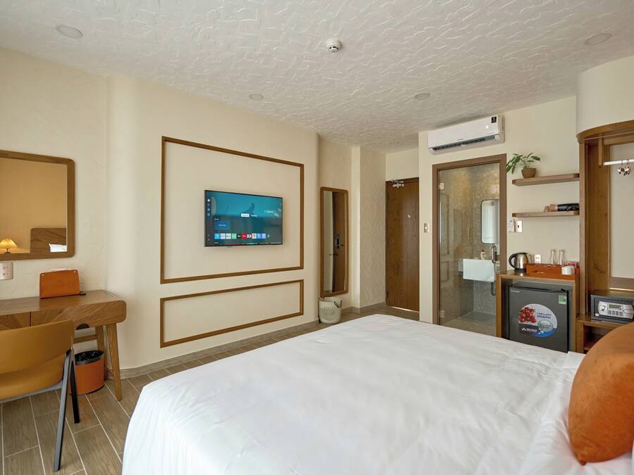 A hotel room with a bed, a desk, a television, a mirror, and a small refrigerator.