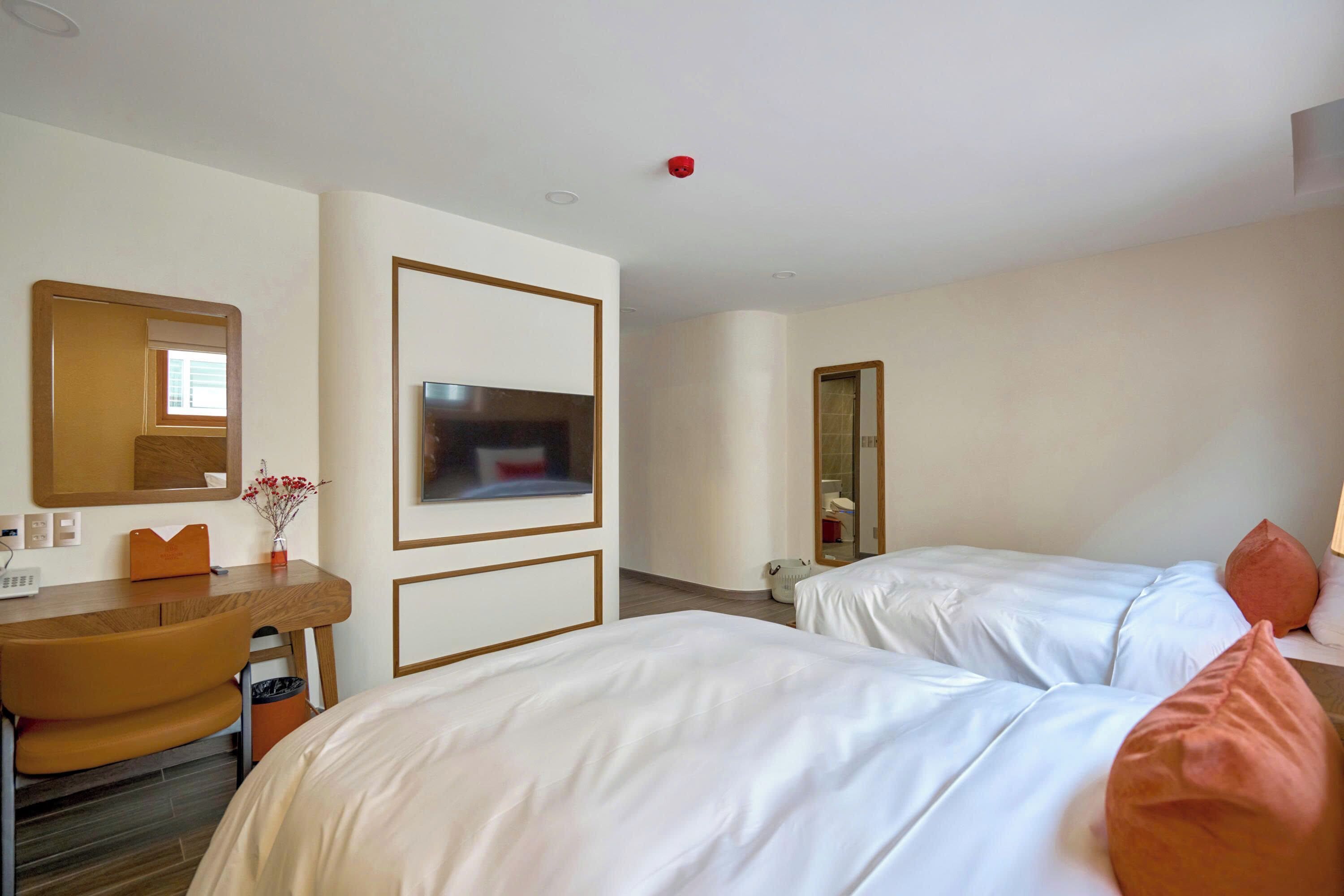 Una habitación de hotel con dos camas, un escritorio, una silla, un televisor y un espejo.