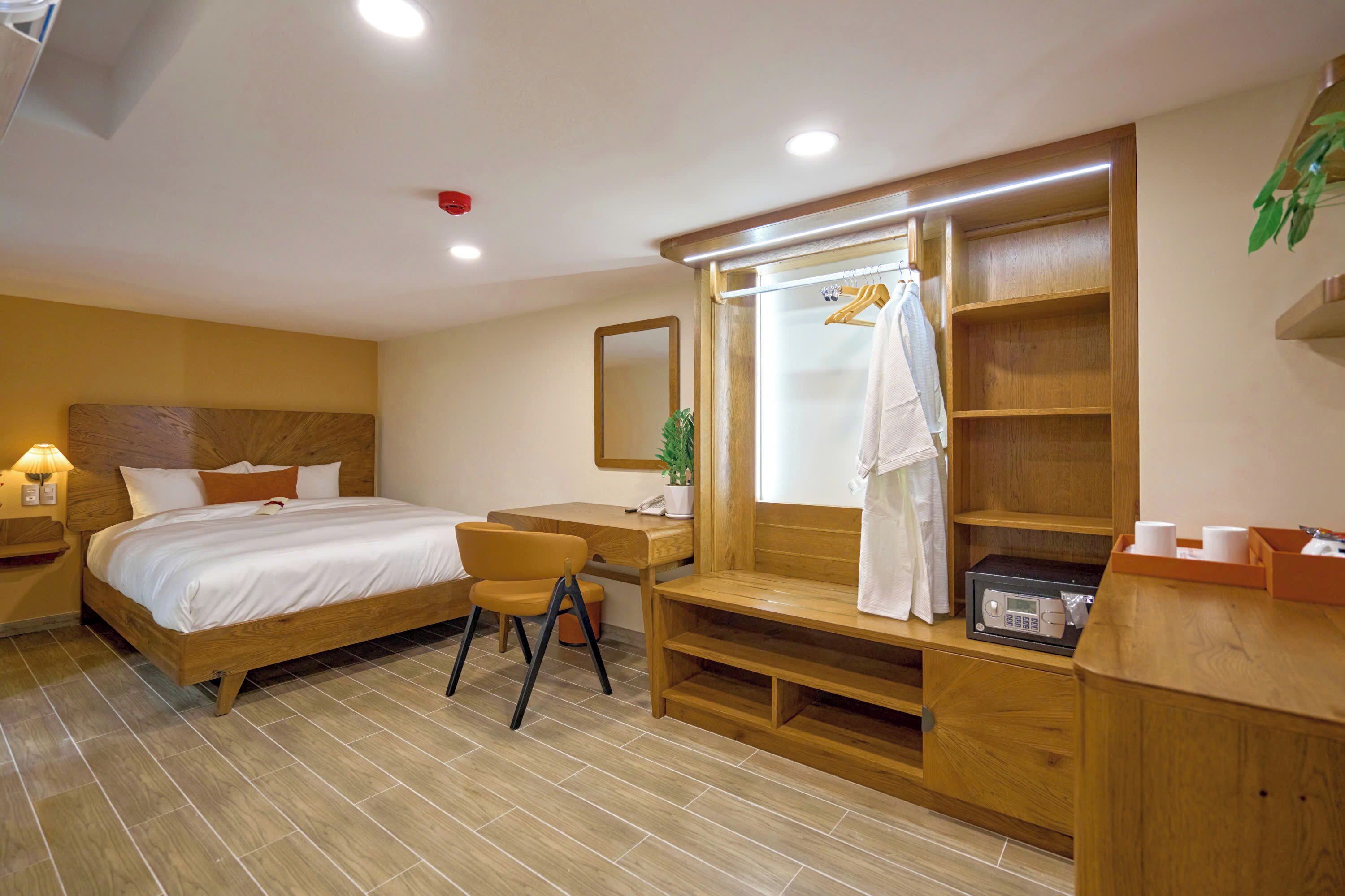 Une chambre d’hôtel équipée d’un lit, d’un bureau, d’une chaise, d’un miroir, d’un peignoir et d’une étagère contenant des articles de toilette.