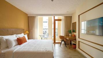 A hotel room with a large bed, a desk, a television, and a view of the outside.