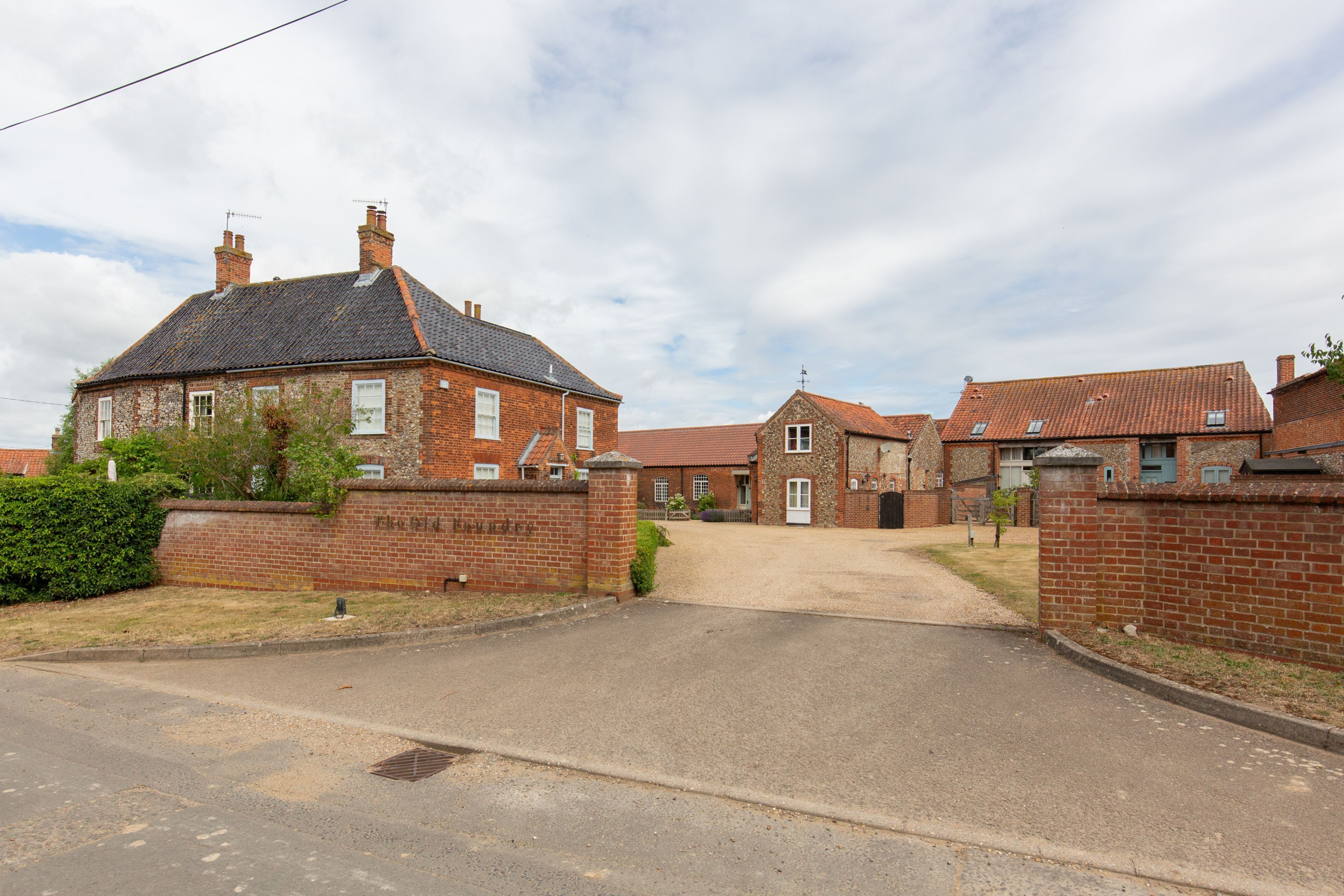 A residential street with brick houses, a gated driveway, and a clear sky.
