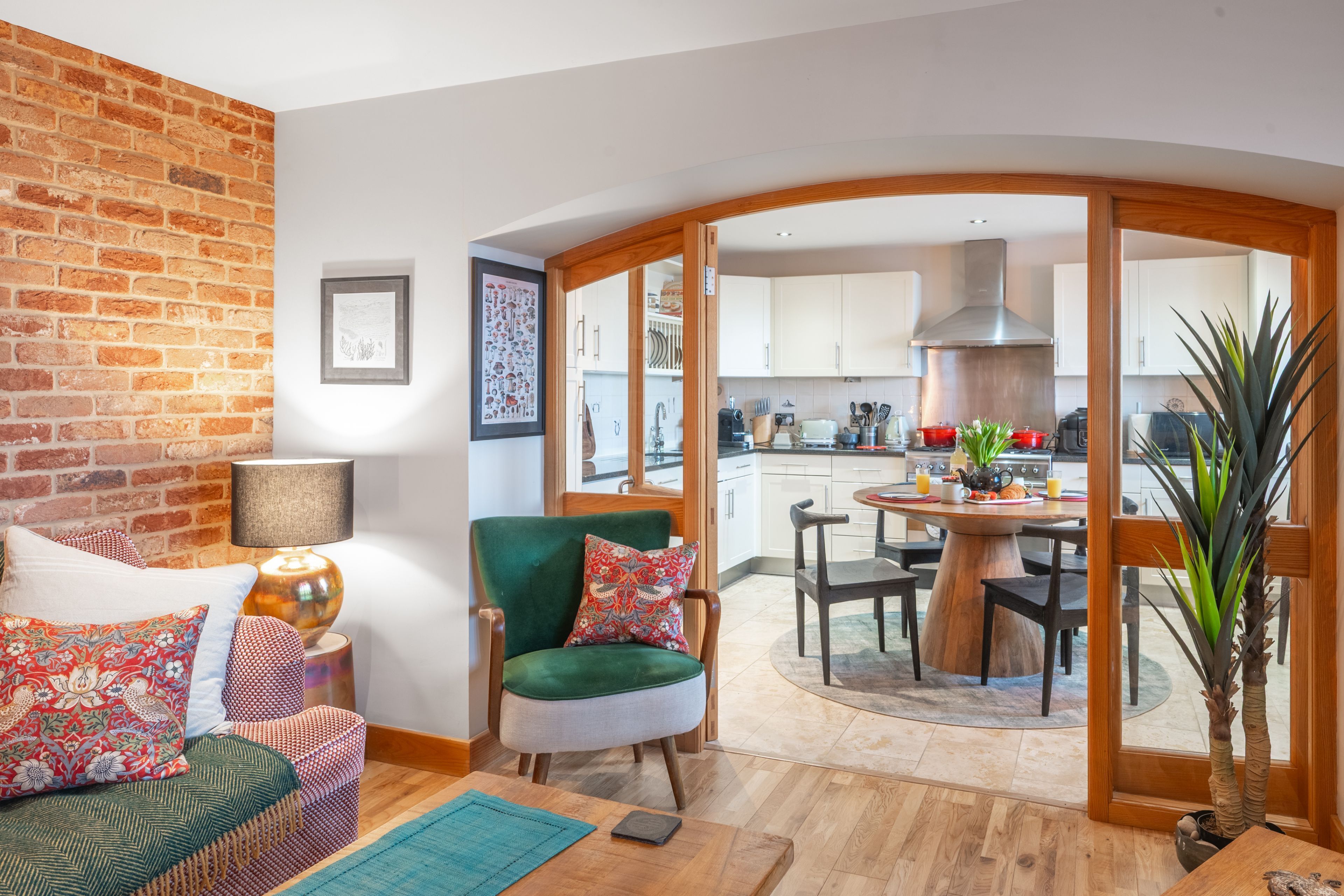 Una sala de estar acogedora con pared de ladrillo, un sillón verde y un comedor con una mesa redonda y sillas.