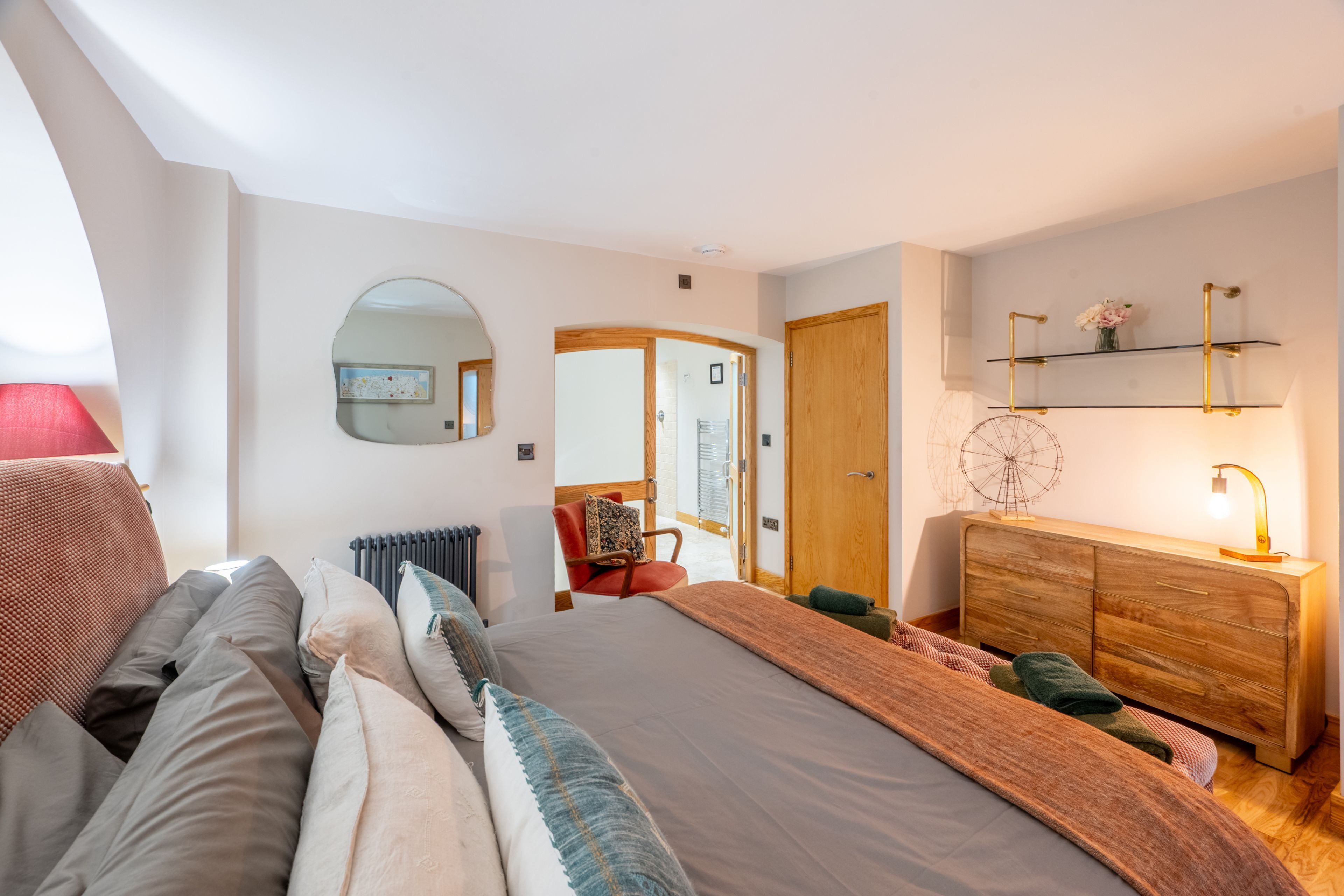 A modern bedroom with a large bed, a wooden dresser, a mirror, and a small desk.