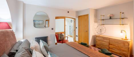 A modern bedroom with a large bed, a wooden dresser, a mirror, and a small desk.
