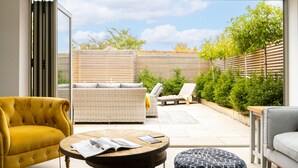 Een moderne patio met een gele bank, een grijze bank en een ronde tafel met tijdschriften.