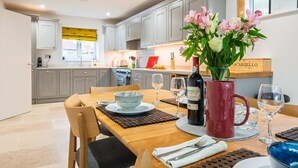 Een moderne keuken met grijze kastjes, een houten eettafel en een bloemenvaas.