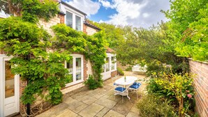 A brick house with a garden patio, a white door, and a white window. - Littlefold, Brancaster, Norfolk (Brancaster)