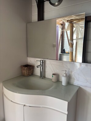 A bathroom with a white sink, a mirror, a wicker basket, and a soap dispenser. - Moonlodge – Ocean-view ecolodge with private hot tub, beach within walking distance (Sainte-Luce)