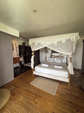A bedroom with a canopy bed, wooden flooring, and a small rug. - Bwaflo – Lodge with a hot tub in Martinique, an outdoor kitchen, and a beach within walking distance   (Sainte-Luce)