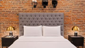 Una cama con cabecera capitonada, dos mesitas de noche con lámparas, y tres cascos en la pared.
