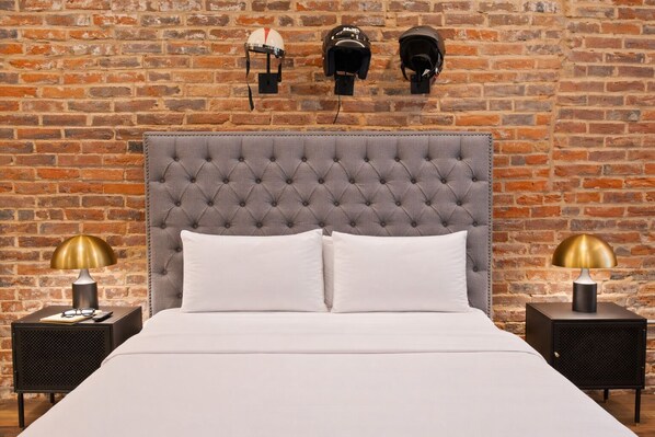 A bed with a tufted headboard, two bedside tables with lamps, and three helmets on the wall.
