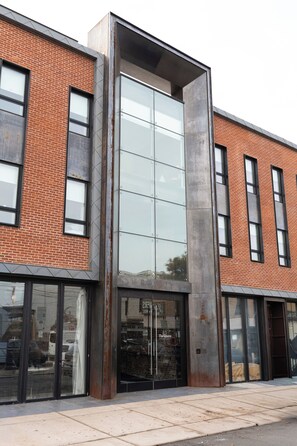 A modern building with large glass windows, a brick facade, and a metal structure. - Sosuite at The Queen - Queen Village (Philadelphia)