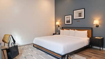 Una camera d'albergo con un letto, comodini, lampade a parete, una sedia, una borsa e un paio di stivali.
