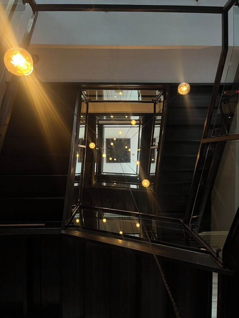 A modern interior with a glass staircase and a central square with hanging lights.