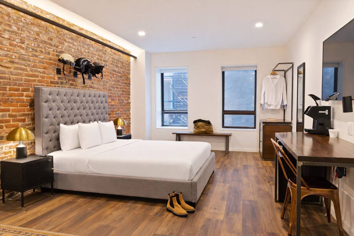 A modern hotel room with a brick wall, a large bed, a desk, and a coffee machine.