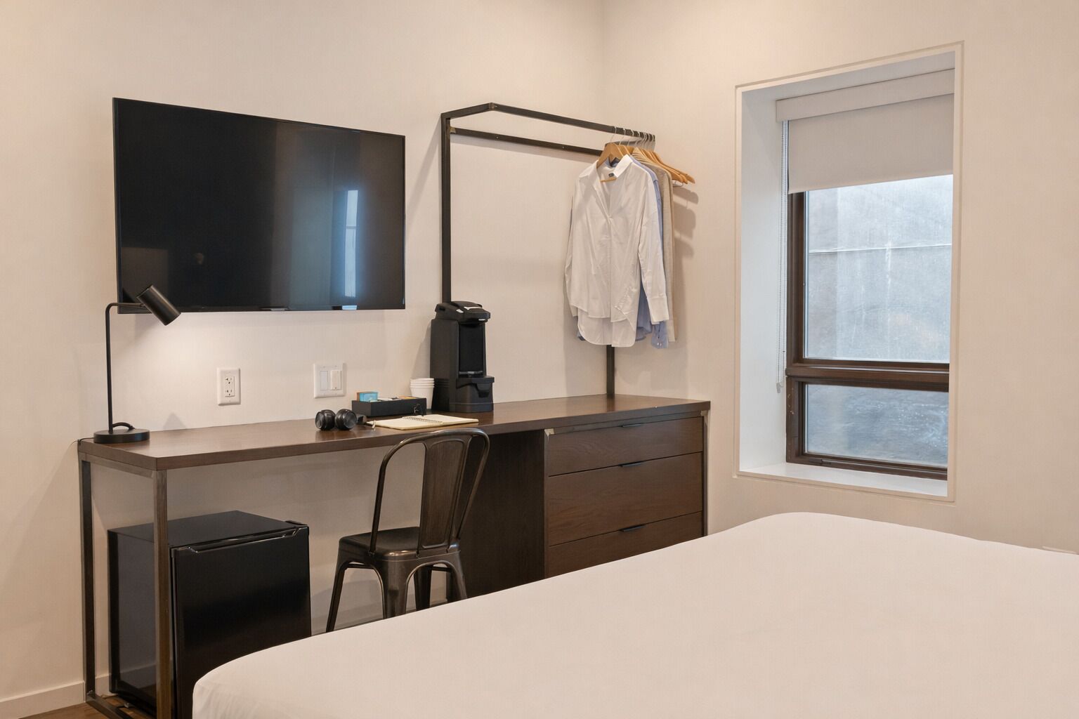 Une chambre à coucher avec un lit, un bureau et une chaise, une télévision, une machine à café et une fenêtre.