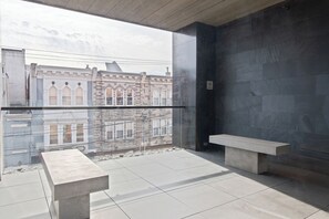 A modern balcony with a clear view of historic buildings, a glass railing, and a stone wall. - Sosuite at The Queen - Queen Village (Philadelphia)