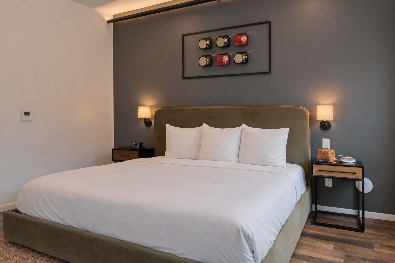 A neatly arranged bedroom with a large bed, two bedside tables, a wall-mounted lamp, and a framed picture above the bed.