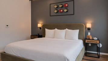 A neatly arranged bedroom with a large bed, two bedside tables, a wall-mounted lamp, and a framed picture above the bed.