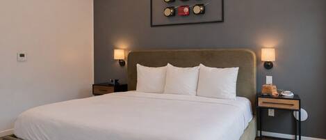 A neatly arranged bedroom with a large bed, two bedside tables, a wall-mounted lamp, and a framed picture above the bed.