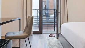 Ett modernt hotellrum med en säng, en stol, ett skrivbord och en balkong med gardiner.