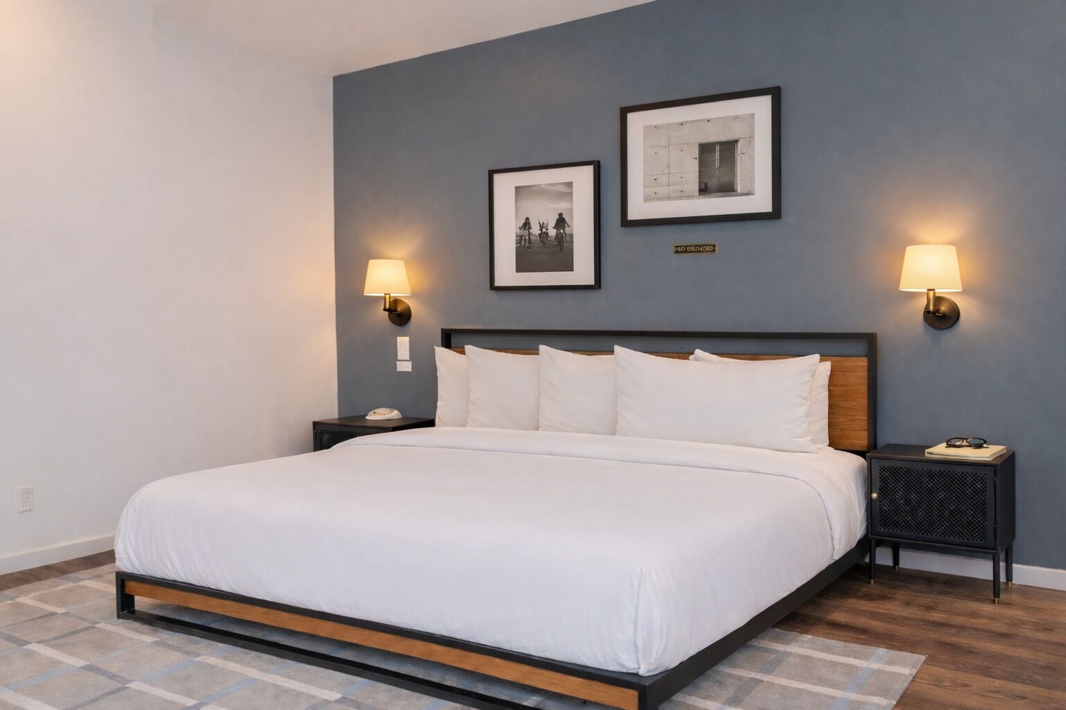 A hotel room with a large bed, two nightstands, two wall-mounted lamps, and two framed pictures on the wall.