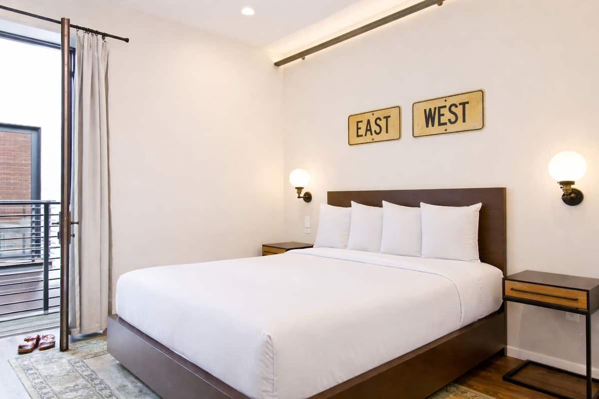 A hotel room with a large bed, two bedside tables, a headboard, and a view of the outside.