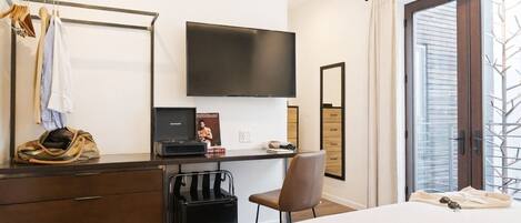 Un dormitorio con cama, escritorio con computadora portátil, silla, armario, televisor y ventana con vista.