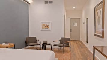 A hotel room with a bed, two armchairs, a small table, a rug, and a door leading to another room.