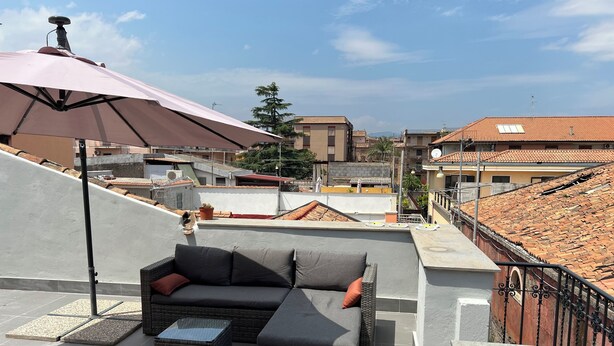 Terraza en la azotea con un sofá seccional gris, una mesita y un paraguas grande.