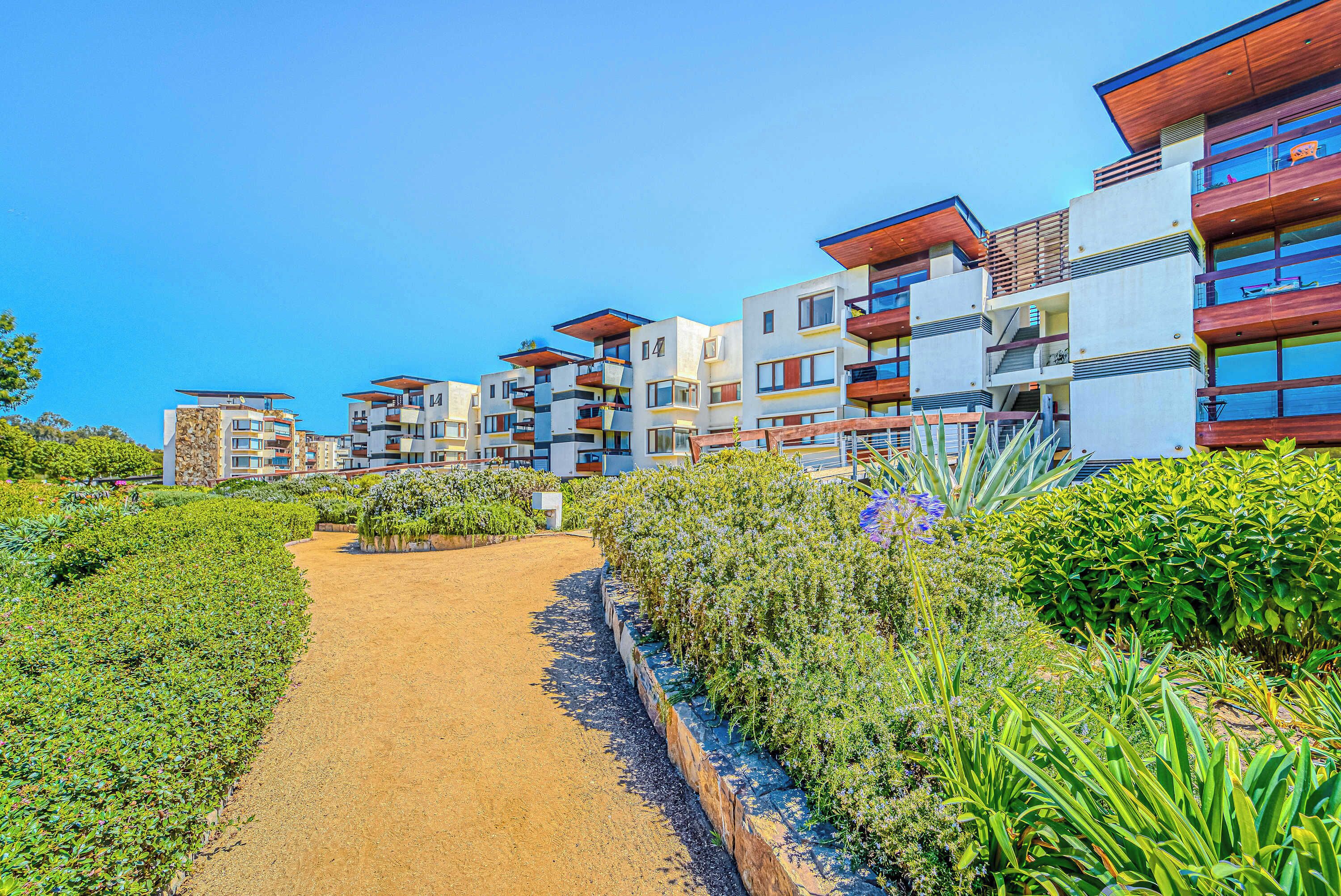 A modern residential complex with multiple balconies, a central pathway, and lush greenery.