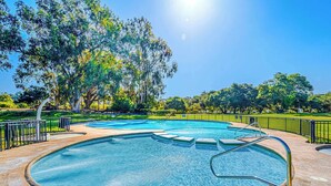 Una piscina circular con barandilla de metal, rodeada por un suelo empedrado y una cerca de metal.