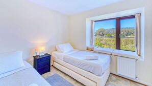 Un dormitorio con dos camas, una mesita de noche, una lámpara y una ventana que ofrece vistas a un paisaje.