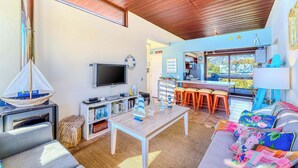 Una sala de estar con televisor, techo de madera, sofá, mesa de centro y vistas al exterior.