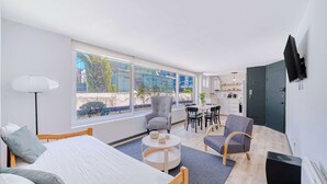 Una habitación de hotel moderna con cama, zona de estar, mesa de comedor y ventanas amplias.