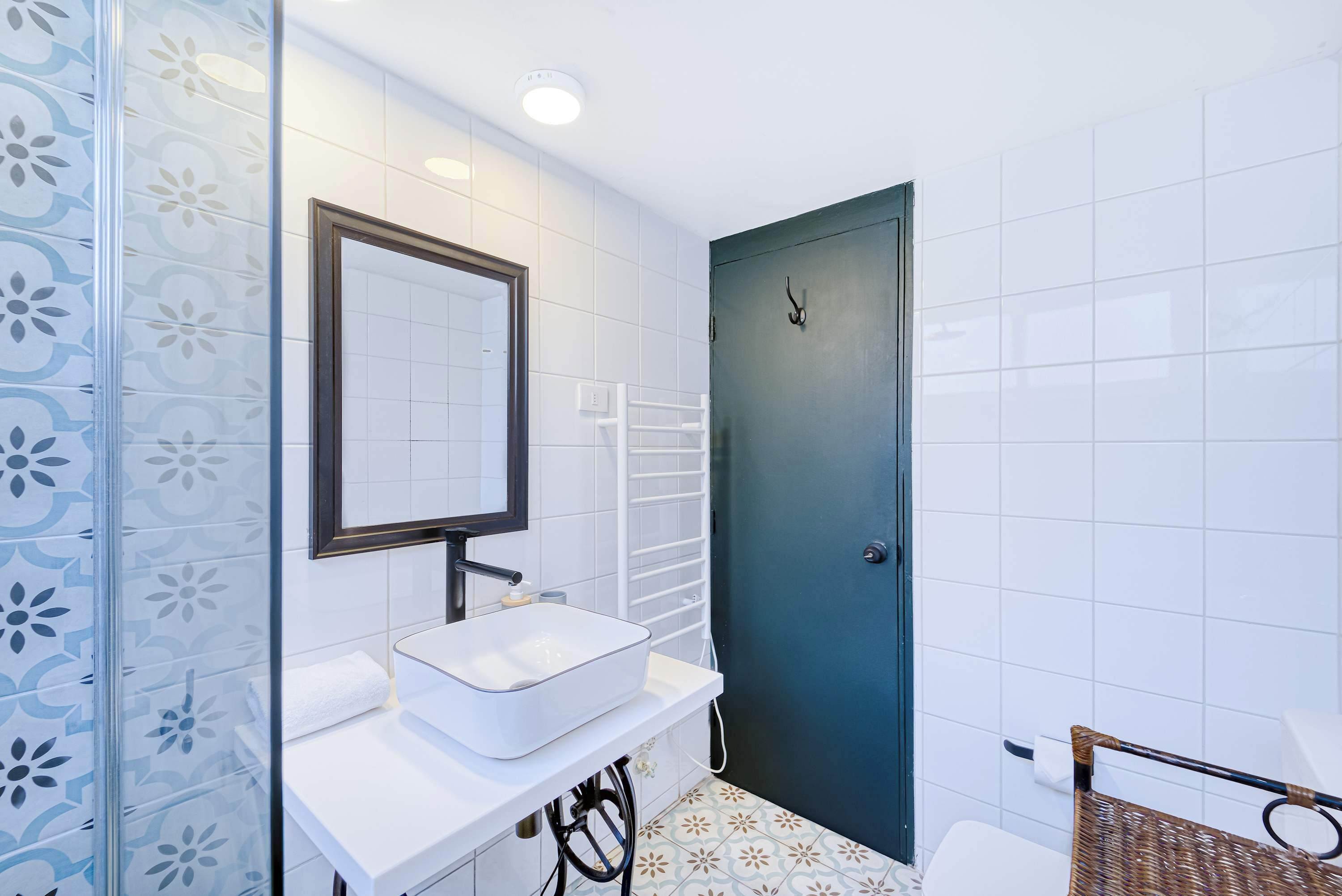 A bathroom with a white sink, a mirror, a towel, a door, and patterned tiles.