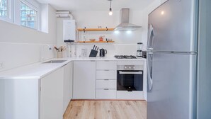 Una cocina moderna con muebles blancos, un refrigerador de acero inoxidable, horno empotrado y estufa a gas.