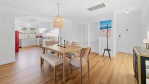 En rummelig spiseplads med et træbord og stole, en hængende lampe samt udsigt til køkken og opholdstue.