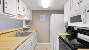 A compact kitchen with white cabinets, a stainless steel sink, a microwave, a stove, and a toaster. - Gulf View 10 by Liquid Life (Gulf Shores)
