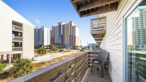 A balcony with a wooden deck, a chair, and a view of high-rise buildings in the background. - Gulf View 10 by Liquid Life (Gulf Shores)